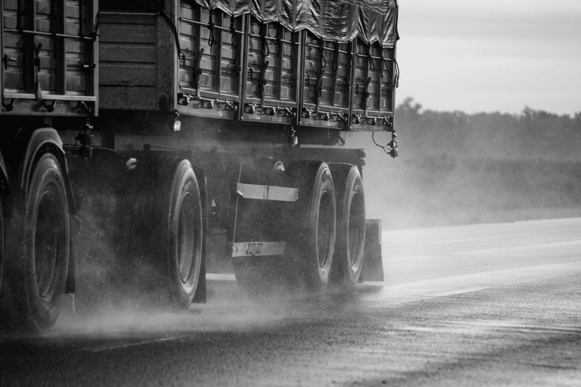 Perspectiva en blanco y negro de un camión transportando alimentos sobre asfalto mojado bajo la lluvia, simbolizando los retos del transporte de alimentos y cambio climático.