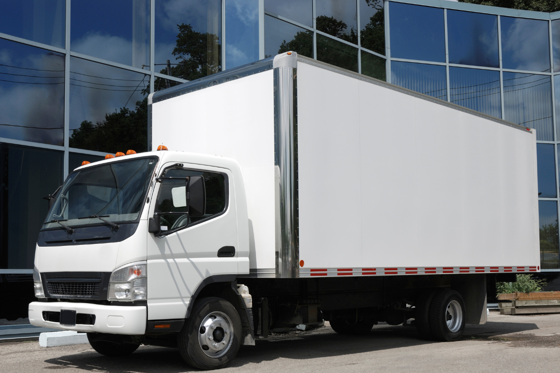 Camión blanco de transporte refrigerado estacionado frente a un edificio.